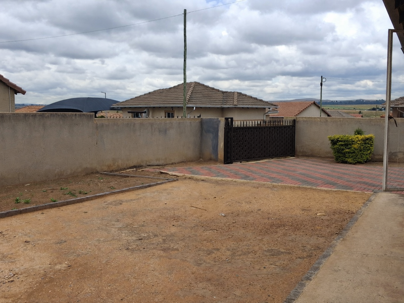 Rear yard area featuring a paved driveway section, metal gate, and boundary walls, with an unlandscaped dirt ground surface.