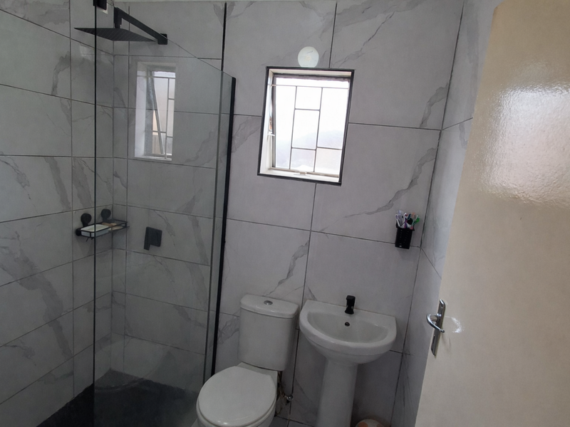Modern bathroom featuring a walk-in shower with a glass screen, rain shower head, pedestal basin, and toilet, finished with contemporary marble-look wall tiles.