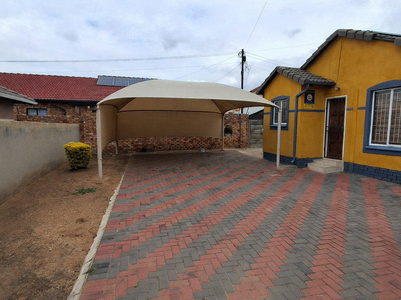 Front exterior view of the property featuring a paved driveway, a shade sail carport, and secure window bars.