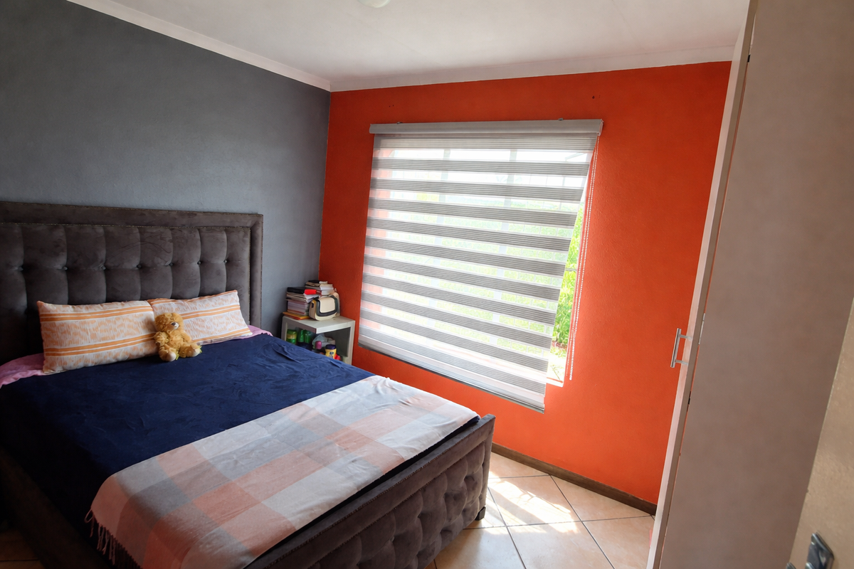 A bedroom featuring tiled flooring, a built-in cupboard, and modern roller blinds, with a bold orange and grey accent wall design.