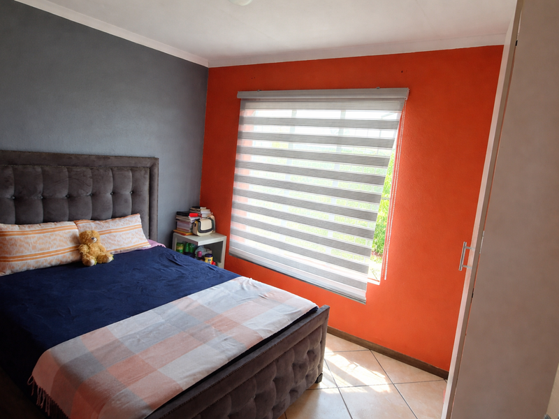 A bedroom featuring tiled flooring, a built-in cupboard, and modern roller blinds, with a bold orange and grey accent wall design.