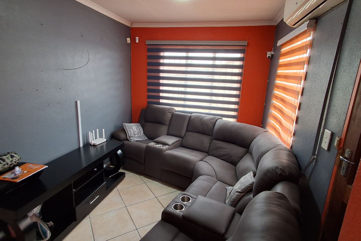 A living room featuring tiled flooring, an air conditioning unit, and dual-tone wall paint with roller blinds.