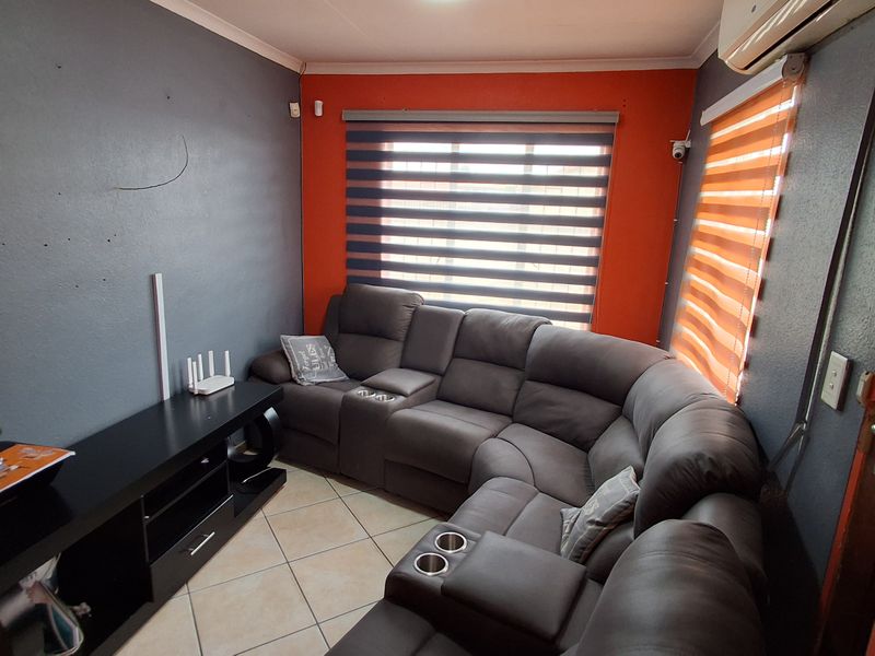 A living room featuring tiled flooring, an air conditioning unit, and dual-tone wall paint with roller blinds.