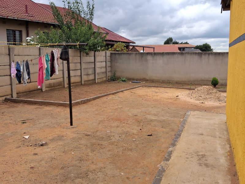 A rear yard area featuring a precast concrete boundary wall, concrete pathway, and an unlandscaped dirt surface ready for garden development.
