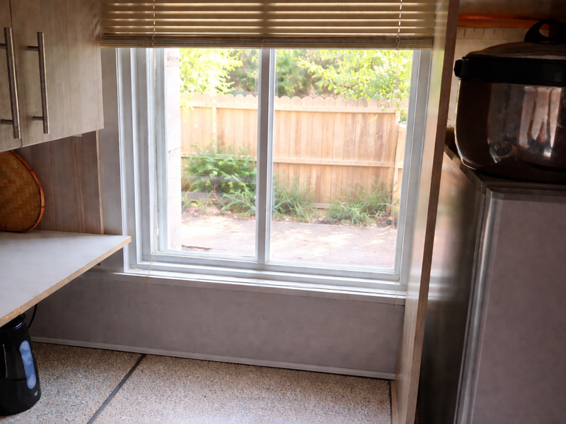 A functional kitchen area featuring laminate countertops, built-in cabinetry, and a window overlooking the rear garden area.