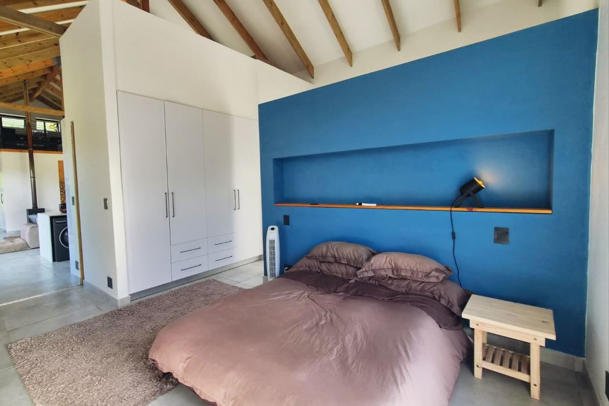 Spacious bedroom featuring a high vaulted timber ceiling, built-in wardrobe storage, and a distinctive blue accent wall with a recessed display niche.