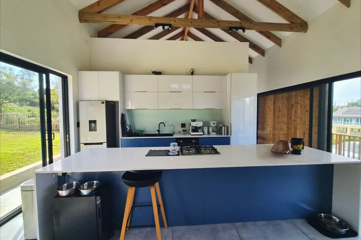 Modern kitchen featuring a large island with gas hob, sleek cabinetry, and exposed timber roof trusses, opening onto an outdoor area via sliding doors.