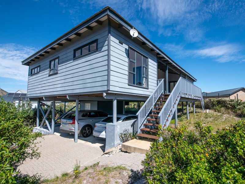 Elevated stilted house featuring timber cladding, an external staircase leading to the main entrance, and a covered ground-level parking area.