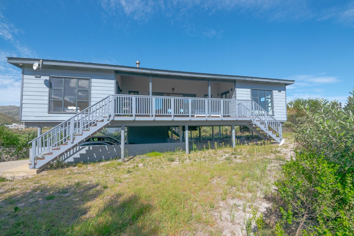 Rear view of a raised house featuring a spacious timber deck, dual staircases, and weatherboard cladding, set above an unlandscaped garden area.