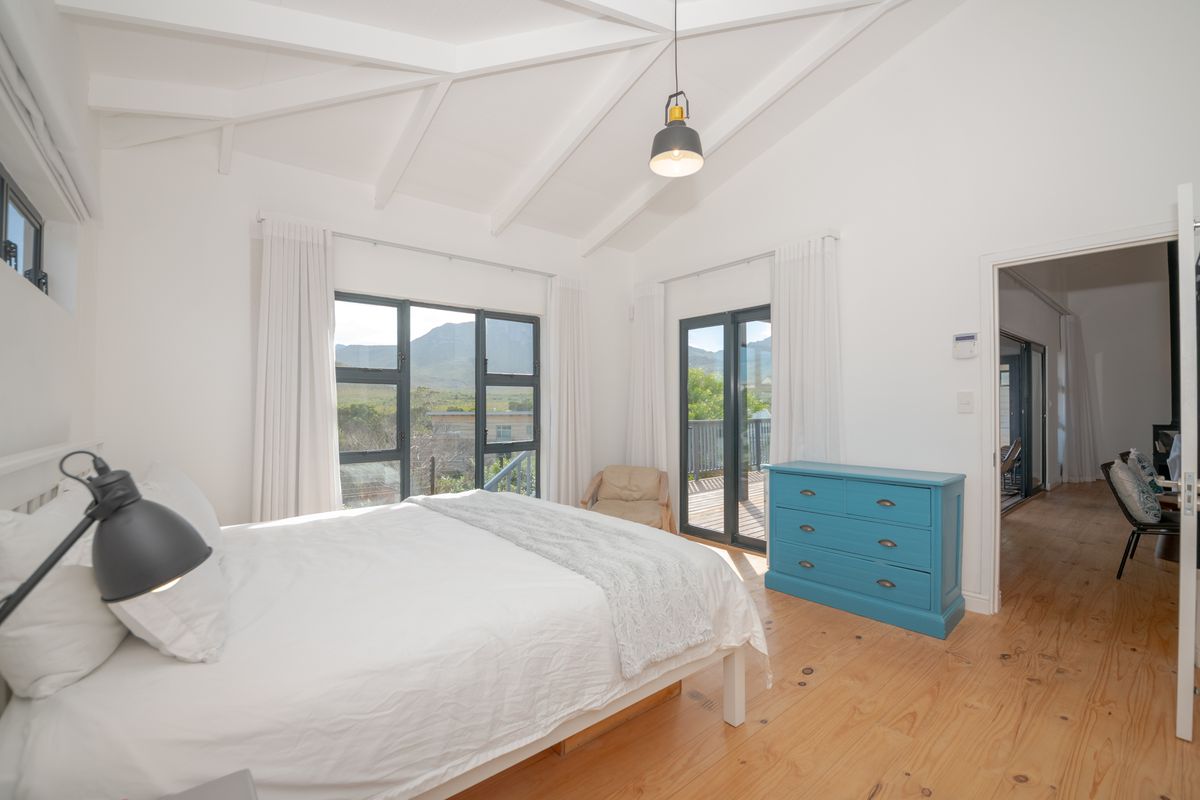 Spacious bedroom featuring vaulted ceilings with exposed rafters, timber flooring, and large windows providing natural light and access to an outdoor deck.