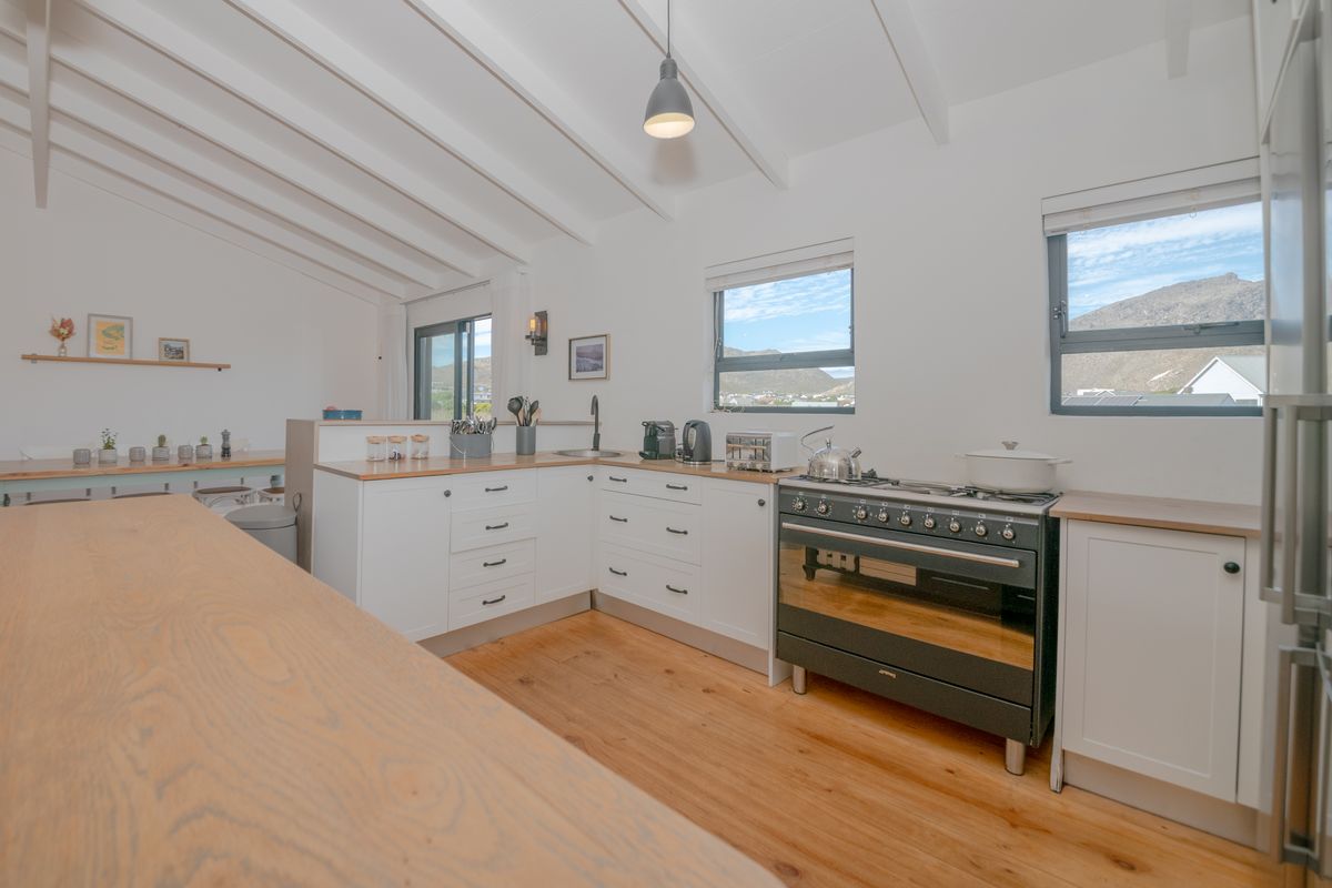 A bright, modern kitchen featuring timber flooring, exposed beam ceilings, wooden countertops, and a professional-style freestanding gas stove with mountain views.