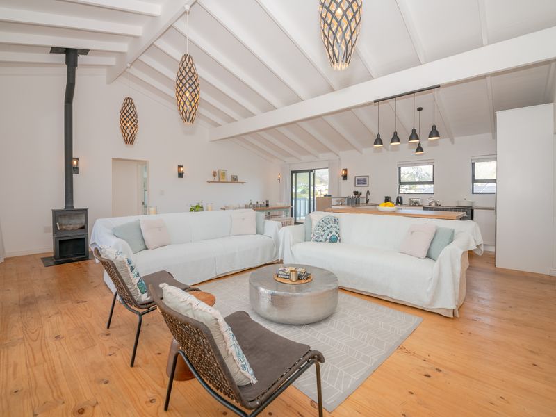 Spacious open-plan living area featuring vaulted ceilings with exposed beams, timber flooring, a cozy wood-burning fireplace, and a modern kitchen with a central island.