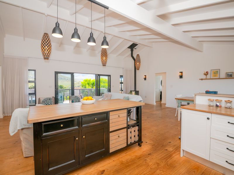 Spacious open-plan living area featuring exposed timber beams, hardwood flooring, a central kitchen island, and a fireplace with direct access to the outdoor deck.