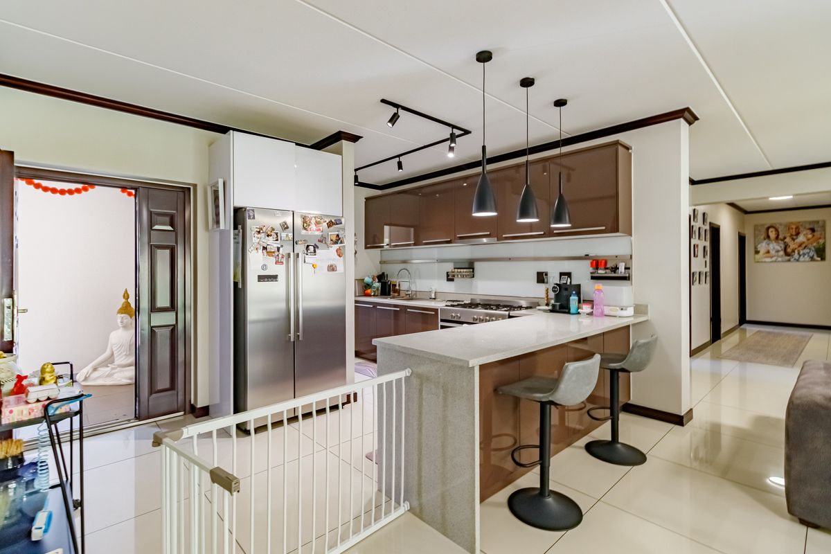 Modern kitchen featuring high-gloss cabinetry, stone breakfast bar, stainless steel appliances, and contemporary pendant lighting, seamlessly integrated into the open-plan living area.
