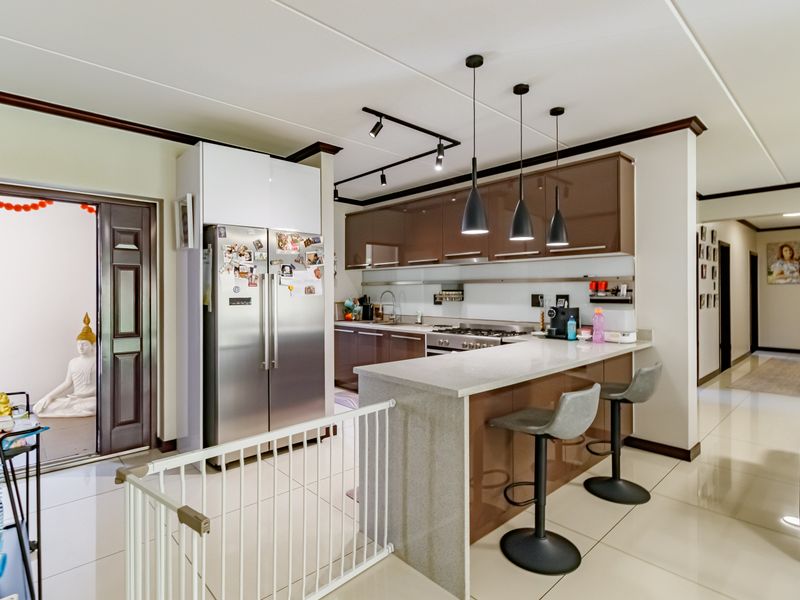 Modern kitchen featuring high-gloss cabinetry, stone breakfast bar, stainless steel appliances, and contemporary pendant lighting, seamlessly integrated into the open-plan living area.