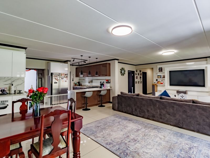 Spacious open-plan living area featuring a modern kitchen with island, integrated appliances, and a dedicated lounge space with built-in media cabinetry.