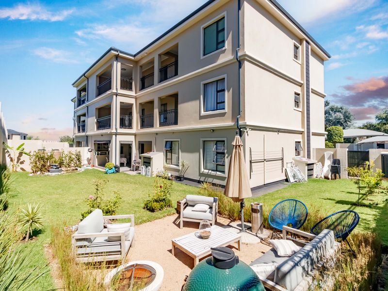 Rear view of a multi-story apartment building featuring private balconies and a well-maintained garden with a gravel patio area.