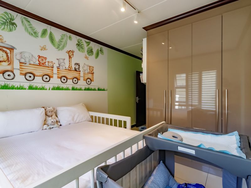 A well-maintained bedroom featuring modern built-in cupboards, tiled flooring, and adjustable track lighting, currently styled as a nursery.