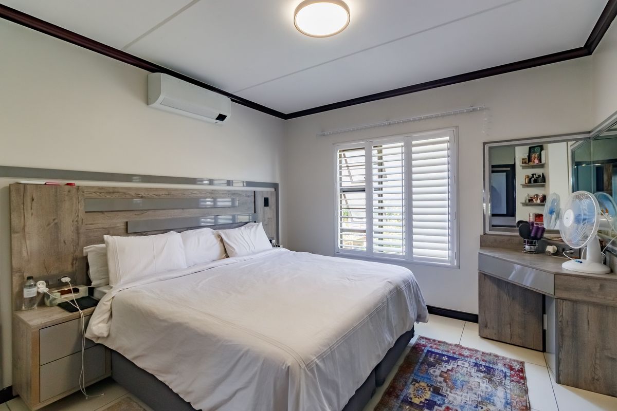 A well-maintained bedroom featuring built-in cabinetry, a custom headboard, integrated vanity, and plantation shutters for light control.