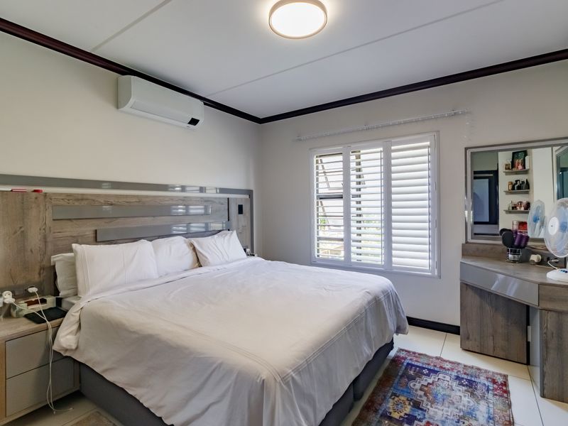 A well-maintained bedroom featuring built-in cabinetry, a custom headboard, integrated vanity, and plantation shutters for light control.