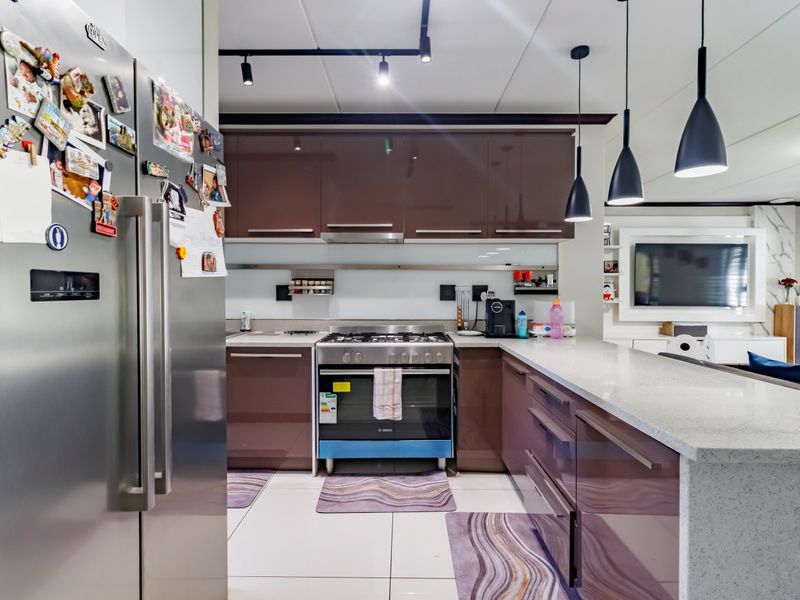 Modern open-plan kitchen featuring high-gloss cabinetry, stone countertops, a gas stove, and contemporary pendant lighting, seamlessly flowing into the living area.