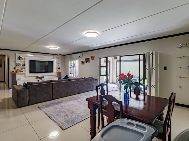Spacious open-plan living and dining area featuring large format floor tiles, built-in media cabinetry, and sliding glass doors leading to an outdoor patio.