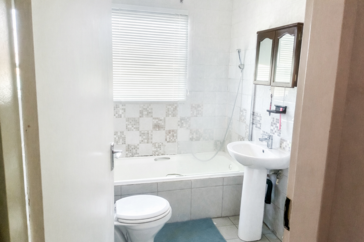 A functional bathroom featuring a pedestal washbasin, a bathtub with shower mixer, and tiled finishes, offering a practical layout for daily use.