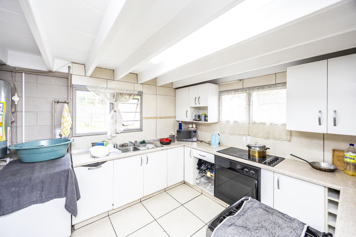 A functional kitchen featuring white cabinetry, a double bowl sink, built-in oven, and ceramic hob, with tiled flooring and exposed beam ceiling details.