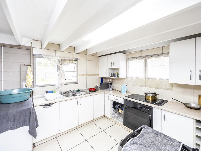 A functional kitchen featuring white cabinetry, a double bowl sink, built-in oven, and ceramic hob, with tiled flooring and exposed beam ceiling details.