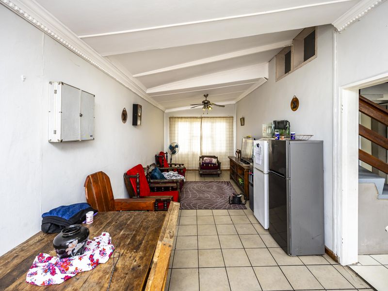 An open-plan living area featuring tiled flooring, a sloped ceiling with a fan, and coved cornicing, offering a functional space for renovation.