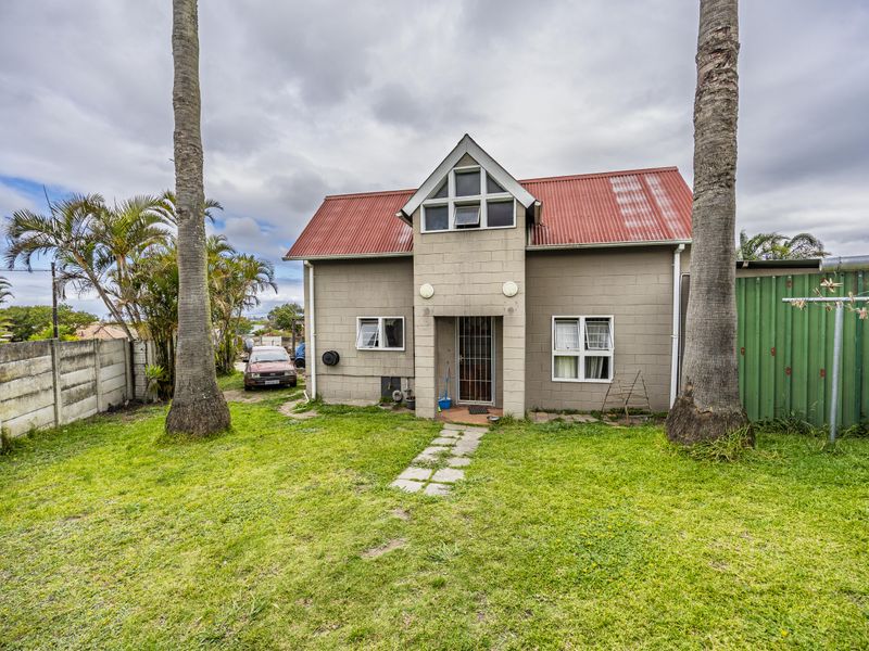 Rear view of a two-story house featuring concrete block construction, a red corrugated metal roof, and a private garden with mature palm trees.