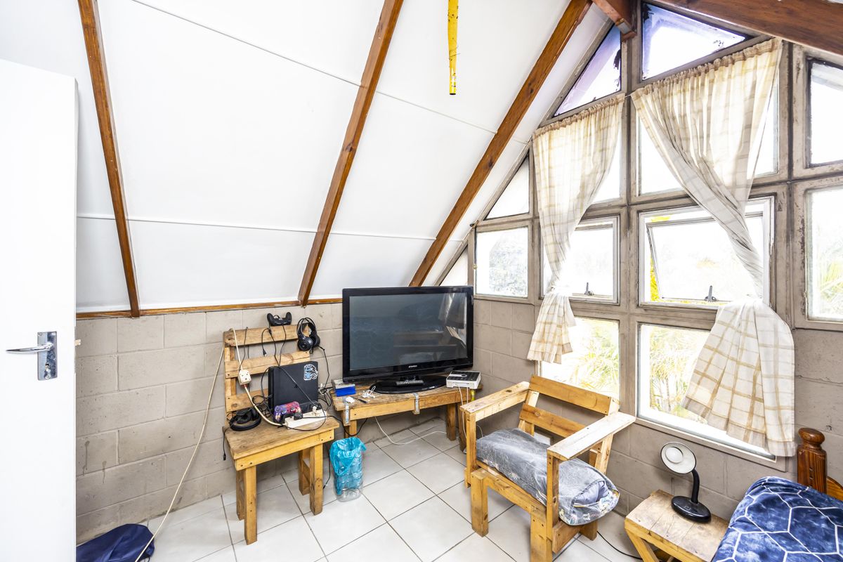 Attic-style living room featuring exposed timber rafters, tiled flooring, and a large multi-pane window providing natural light.