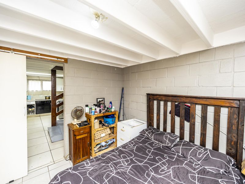 Bedroom featuring exposed beam ceilings and painted concrete block walls, with an adjacent view into the kitchen area.