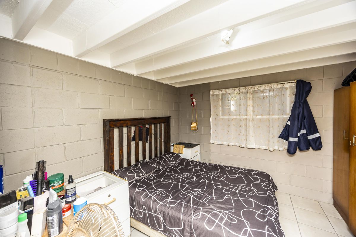 A bedroom featuring exposed beam ceilings, cinder block walls, and tiled flooring, offering a functional space with potential for cosmetic updates.