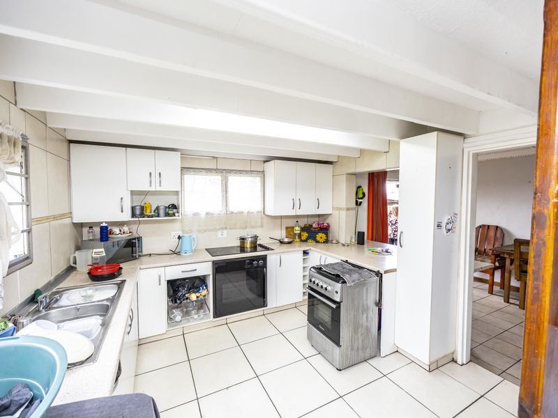 Functional kitchen featuring white cabinetry, tiled countertops, double basin sink, and integrated oven and hob, with exposed ceiling beams and tiled flooring.