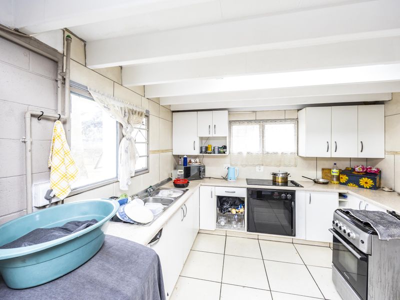 A functional kitchen featuring white cabinetry, tiled flooring, and exposed ceiling beams. The space offers a practical layout with built-in oven and hob.