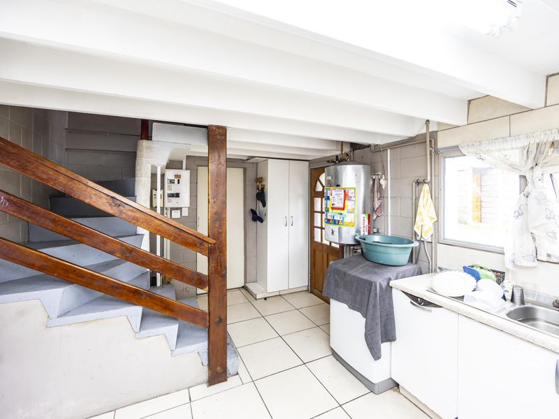 Utility area featuring a staircase, built-in cabinetry, sink, and geyser, with tiled flooring and exposed beam ceiling.
