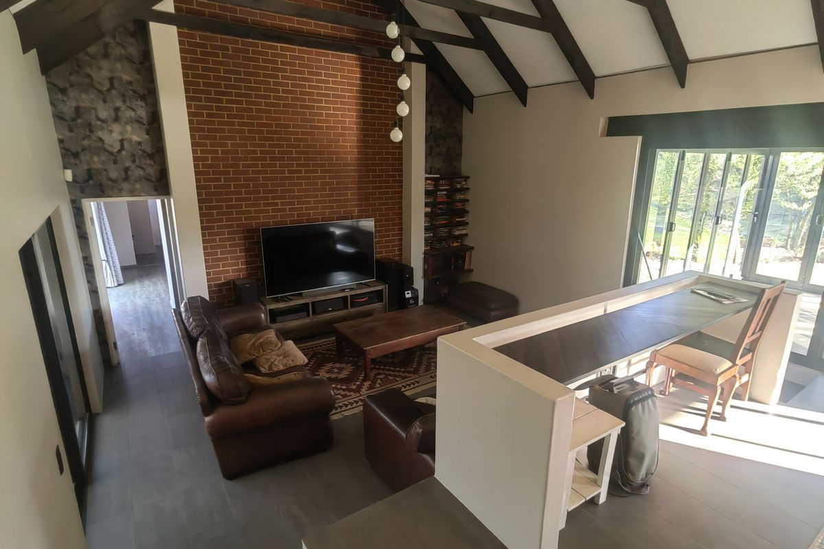 Spacious living room featuring a vaulted ceiling with exposed timber beams, a prominent brick feature wall, and large sliding glass doors leading outdoors.