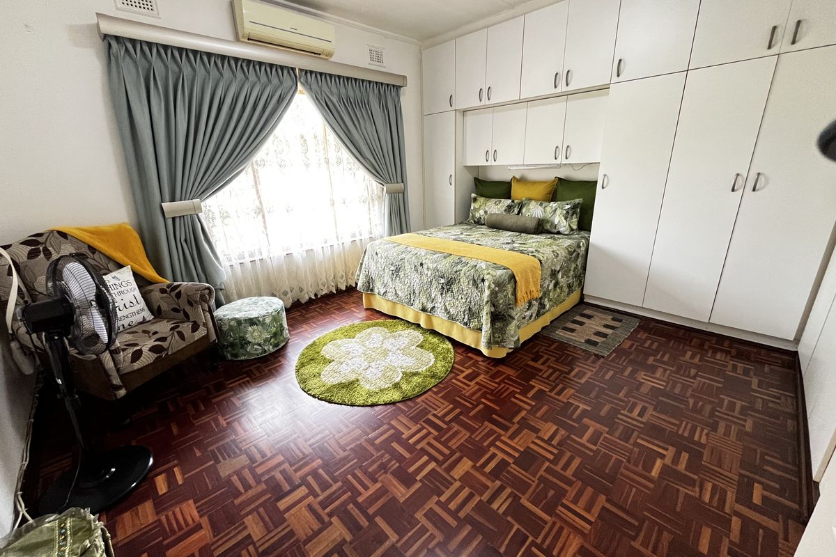 A spacious bedroom featuring classic parquet flooring, extensive built-in cabinetry for storage, and a wall-mounted air conditioning unit.