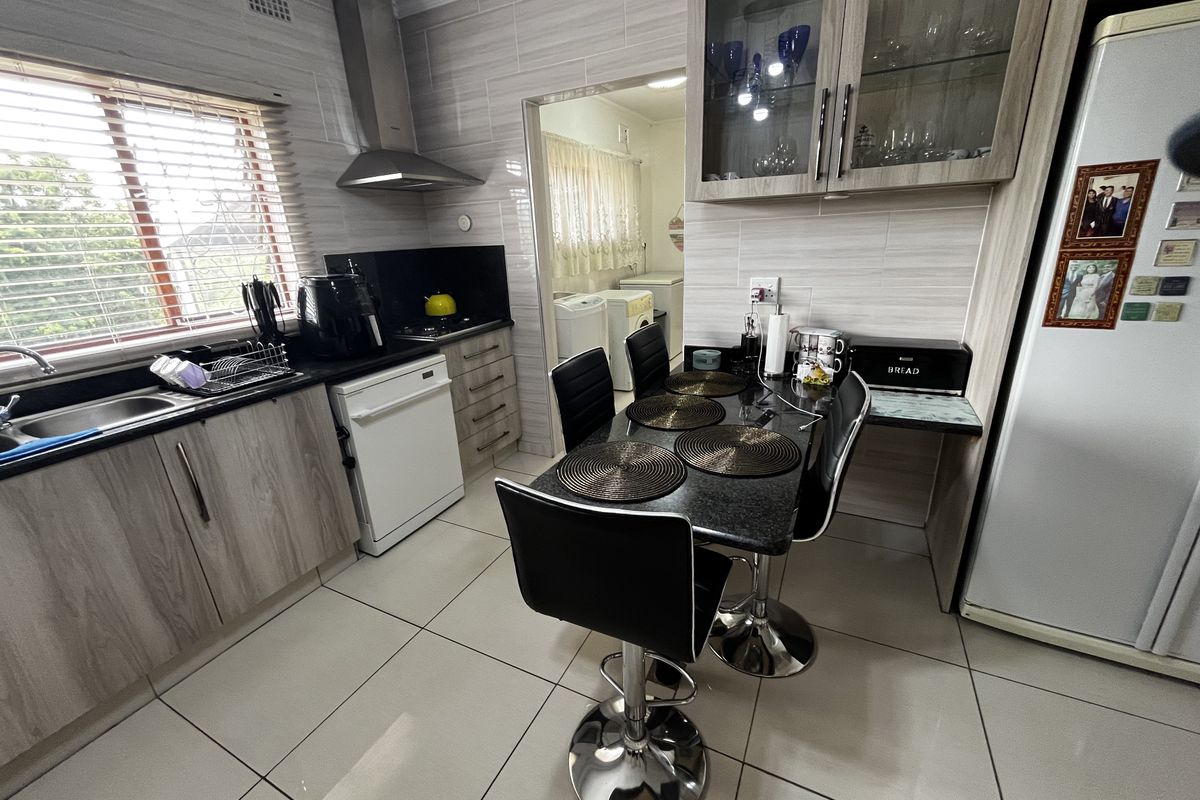 A functional kitchen featuring modern wood-grain cabinetry, tiled finishes, a stainless steel extractor fan, and an integrated dining area with direct access to the laundry.