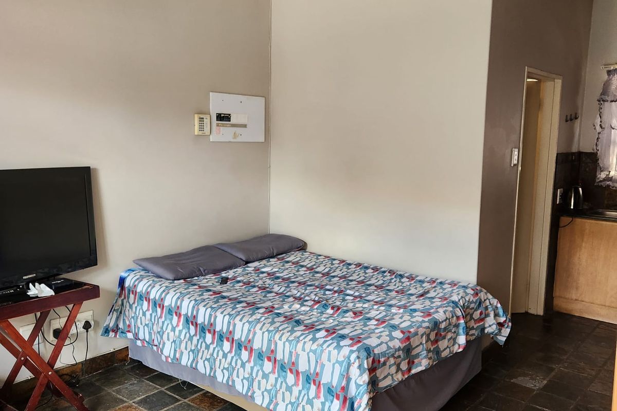 A bedroom featuring stone tile flooring and an integrated electrical distribution board, with direct access to an adjacent kitchen area.