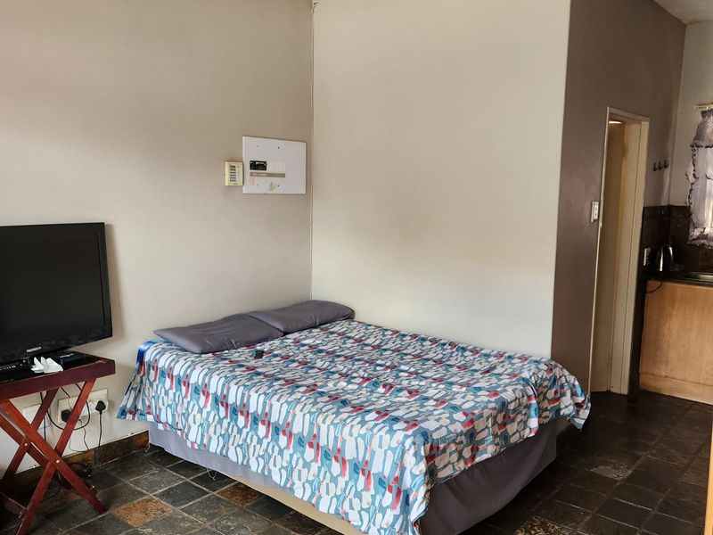 A bedroom featuring stone tile flooring and an integrated electrical distribution board, with direct access to an adjacent kitchen area.