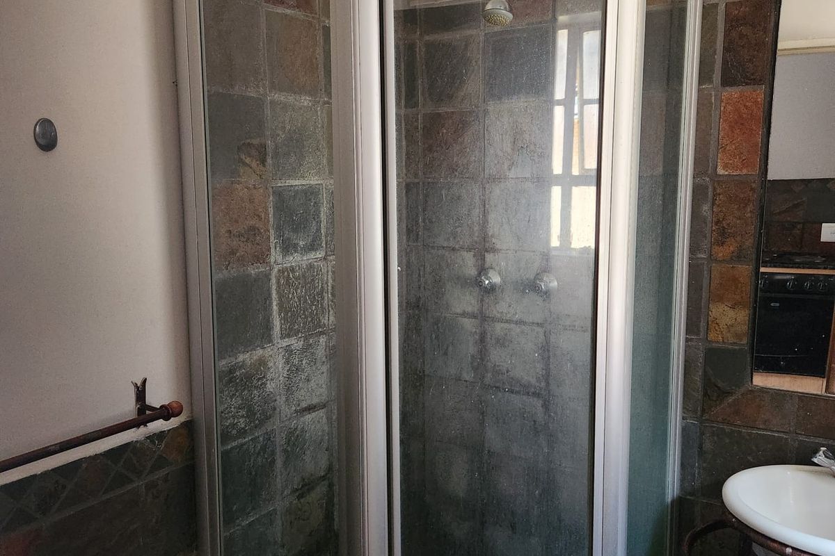 A compact bathroom featuring a corner shower enclosure with tiled walls and a wall-mounted basin, requiring cosmetic updates to modernize the space.