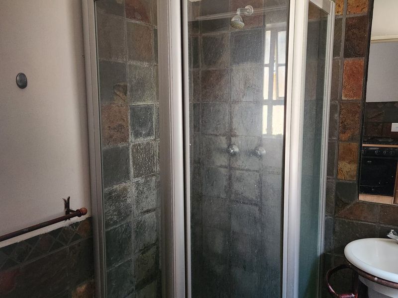 A compact bathroom featuring a corner shower enclosure with tiled walls and a wall-mounted basin, requiring cosmetic updates to modernize the space.