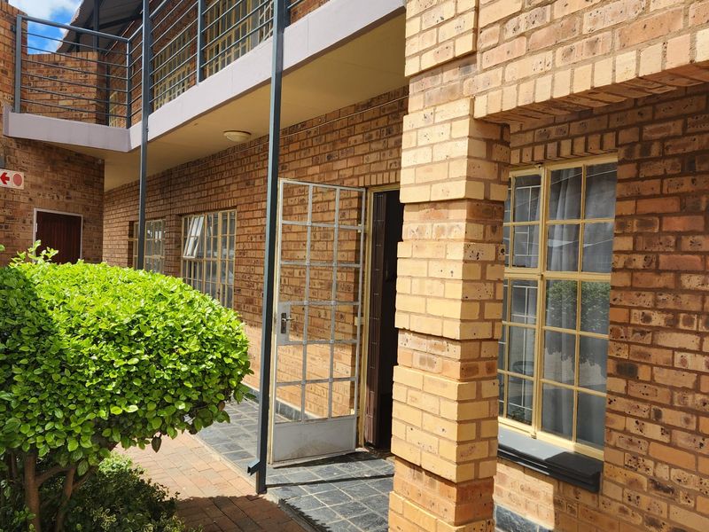 Exterior view of a face brick apartment building featuring a ground-level walkway, metal security gates, and an upper-level balcony with metal railings.