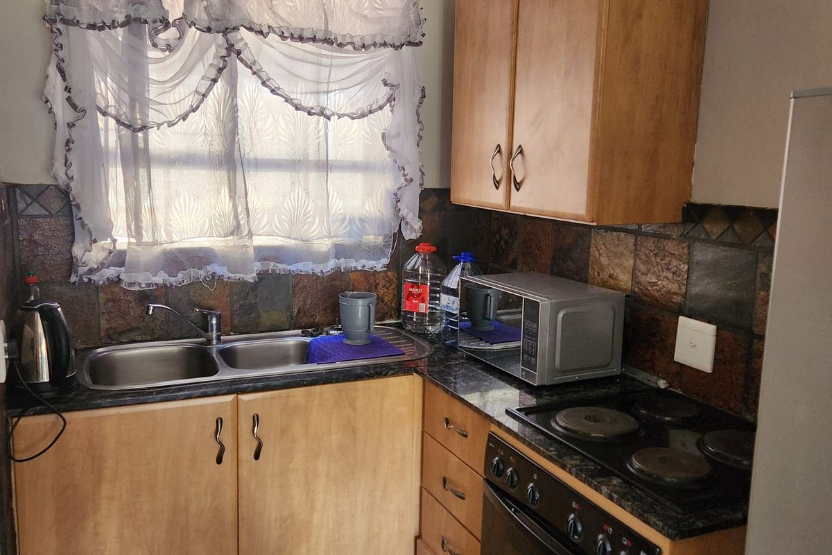 Compact kitchen featuring laminate countertops, built-in oven with electric hob, double bowl sink, and stone tile backsplash with wooden cabinetry.