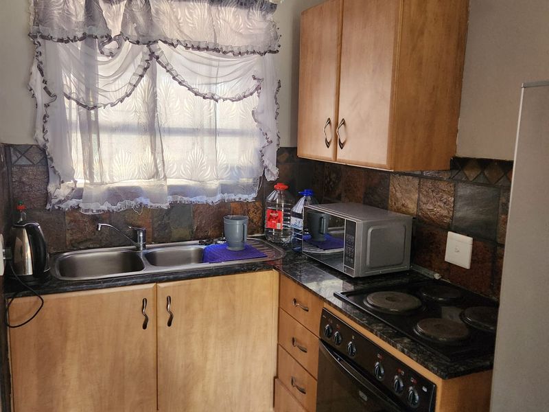 Compact kitchen featuring laminate countertops, built-in oven with electric hob, double bowl sink, and stone tile backsplash with wooden cabinetry.