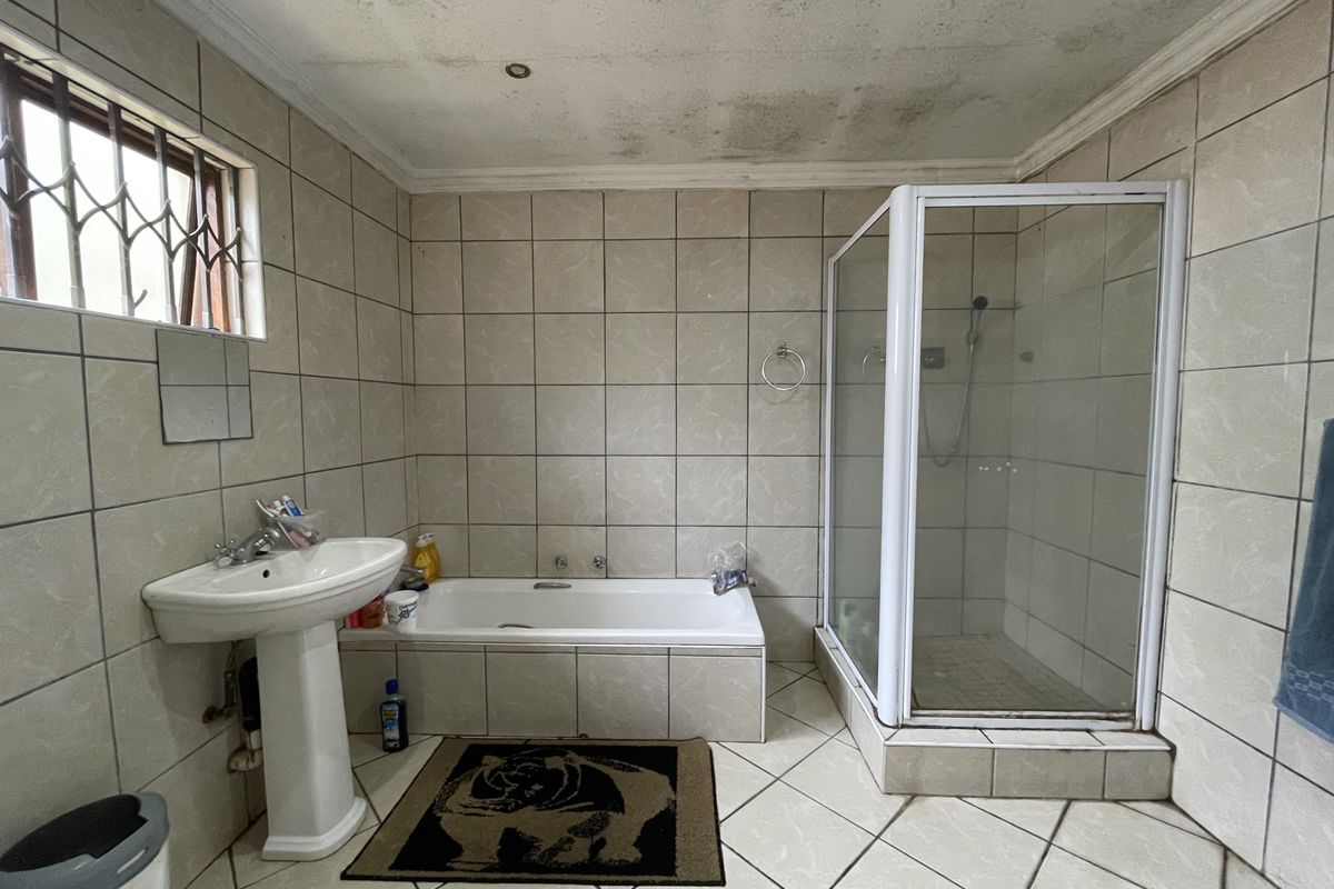 A functional bathroom featuring a pedestal basin, built-in bathtub, and separate shower enclosure, finished with neutral wall and floor tiling.