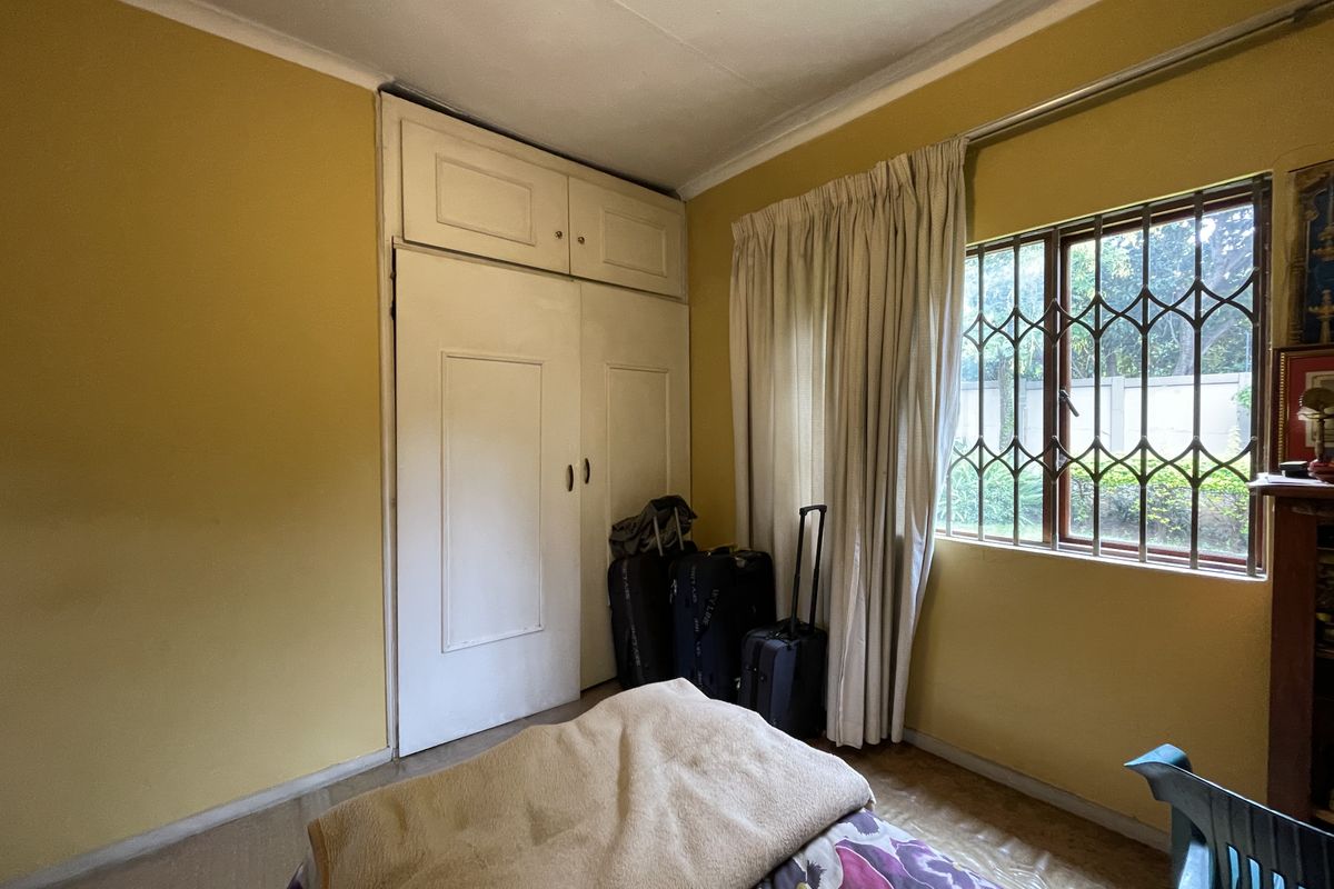 A bedroom featuring built-in cupboards and security bars on the window, requiring cosmetic updates to modernize the space.