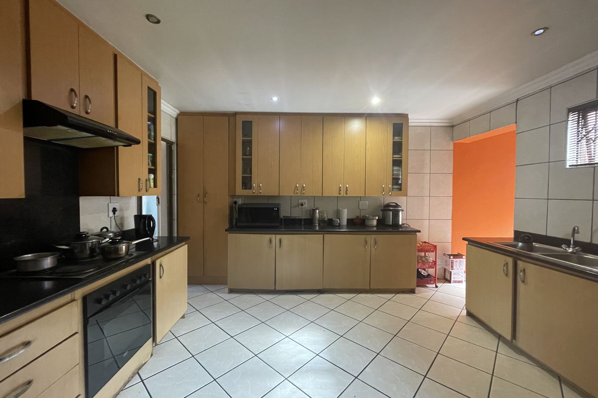A functional kitchen featuring light wood-tone cabinetry, dark countertops, tiled flooring, and integrated appliances, offering a practical layout with ample storage space.
